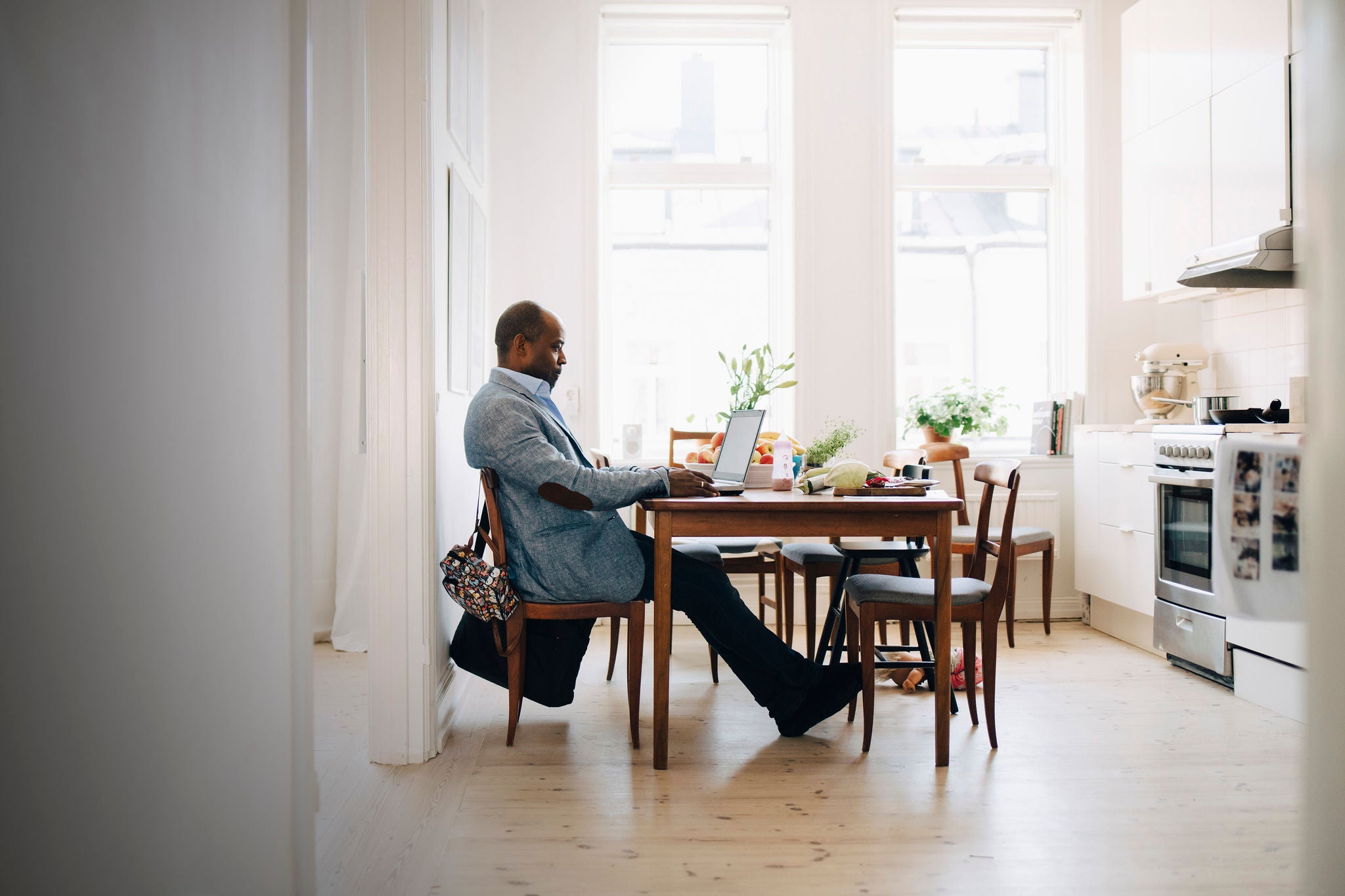 man working on laptop while sitting in kitchen at home