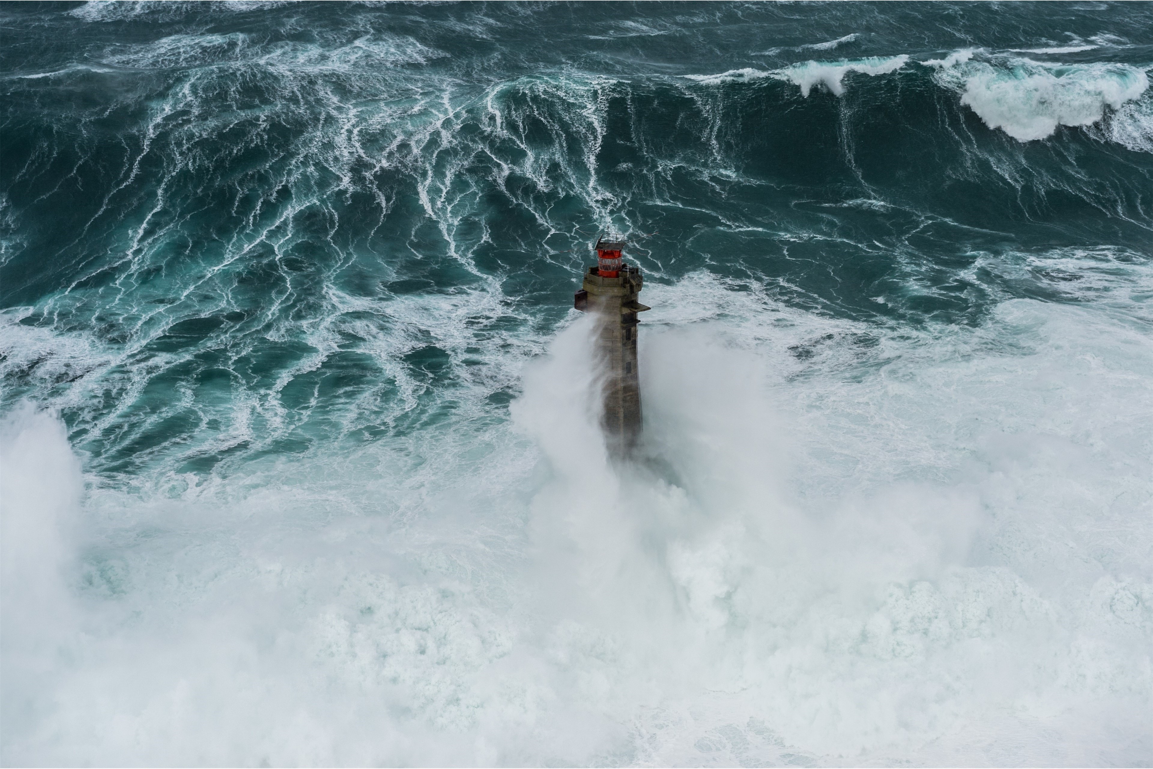 Un phare submergé par des vagues tumultueuses dans une mer agitée.